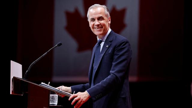 Mark Carney sourit sur une scène. Mark Carney sourit sur une scène.