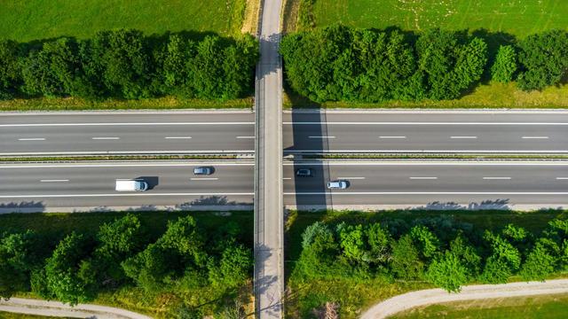 Luftaufnahme einer Brücke über einer Autobahn. Auf der Autobahn fahren vier Autos.
