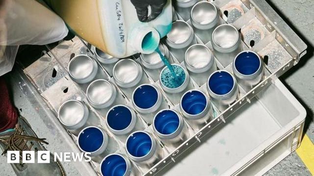 Cans being filled with a blue liquid Cans being filled with a blue liquid