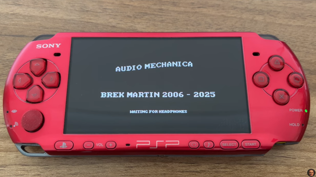 A red Sony PSP gaming console is shown, displaying the lines “Audio Mechanica,” “Brek Martin 2006-2025,” and “Waiting for Headphones.”