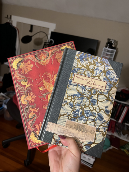 Nala holds up their copy of thousand year old vampire and a fancy red notebook 