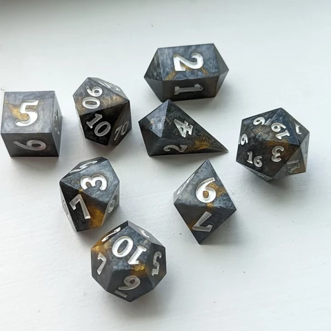 A set of roleplaying dice that are stone-grey with a vein of gold in the center, inked in a pearly white