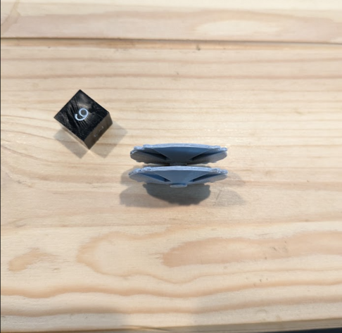 Picture of 3D printed models of a scifi spaceship from the TV show Battlestar Galactica. The model is of a Cylon basestar.  The view is from the side. There is a single black dice behind to show the scale. The model is only a bit bigger than the die!