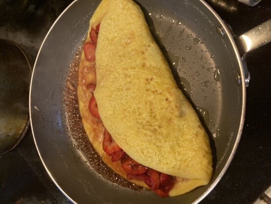 Strawberry omelet in frying pan, the eggs perfectly cooked and the fold over just showing a hint of the strawberries inside 