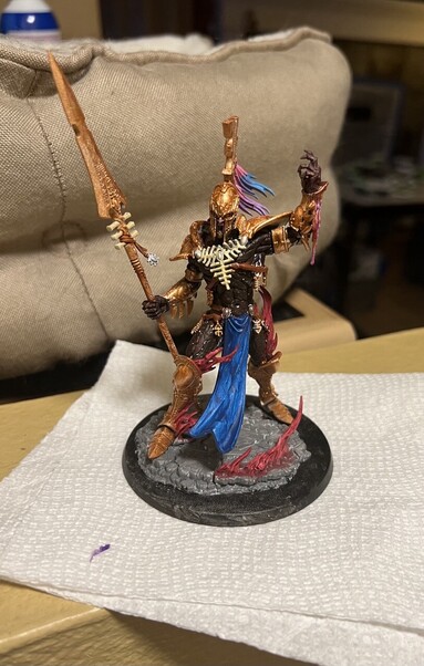 Warhammer 40K miniature

Avatar of Khaine

Bronze armor
Dark brown skin
Blue loin cloth
Pink, blue, and purple hair tassels 
Flames