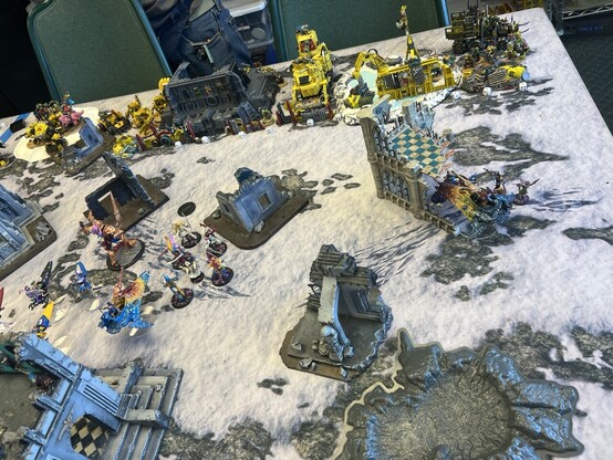Warhammer 40K battle 

Avatar and Wraithblades charge down the center of a snow covered field. 

Jet bikes behind them.

Right flank a squad of harlequins pile out of a Starweaver on an objective. 

Line of yellow orks on the backfield ready for counter charge. 