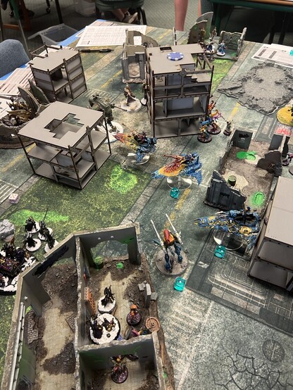 Warhammer 40K Battle

Sisters and Harlequins engaged in battle over an objective in some ruins. 

Wraithlord, Voidweaver, and two Starweavers, damaged from when a knight blew up. Last night approaching, war suits behind building in center. 