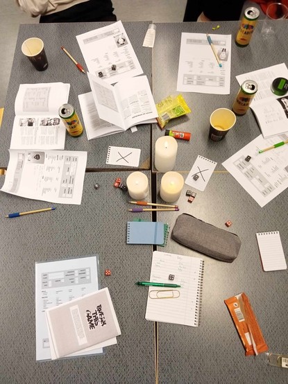 To view of a game table, dice and pens and paper everywhere.