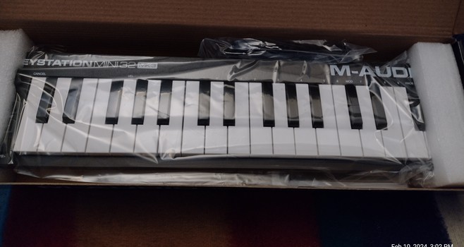 M-Audio Mini Midi M32 Keyboard in a half open box, wrapped in plastic and secured with packing foam end caps.