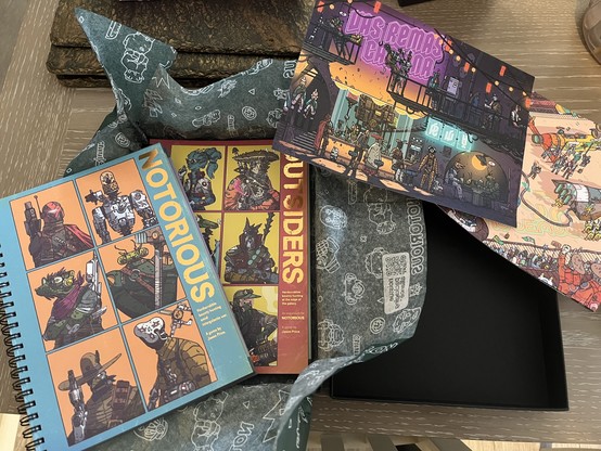 Unboxing of Notorious and Outsiders solo RPG books. The covers each depict Star Wars style bounty hunters, robots, aliens and armoured figures. Also includes two art prints, each depicting bustling SciFi towns.