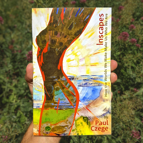 My hand holding a copy of Inscapes. The cover shows an unclothed figure enlivened by a scintillating sunrise.