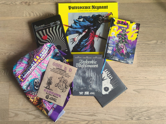 A picture of some TTRPG stuff on a parquet floor. It includes Putrescent Regnant, Death in Space, CY_Borg, Tephrotic Nightmares with an envelope containing game aids, a parody zine with rules to include Garfield themed content in ADnD and an Exalted Funeral bandana with lightnings, skeletons and the brand Funeral Mania.
