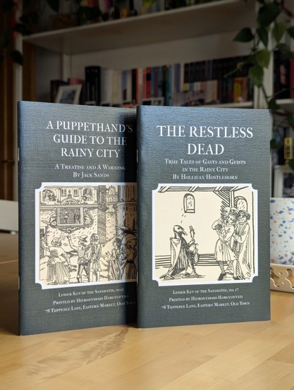 Fotografía de dos suplementos para The Rainy City: A Puppethand's Guide to the Rainy City y The Restless Dead.