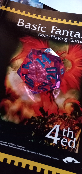 A large, pink D20 sits on the cover of a copy of the Basic Fantasy RPG.