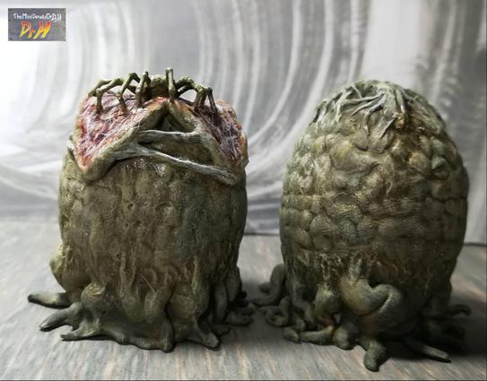 Pair of Alien eggs, one closed, one open with face-hugger crawling out. Low angle photo from the front.