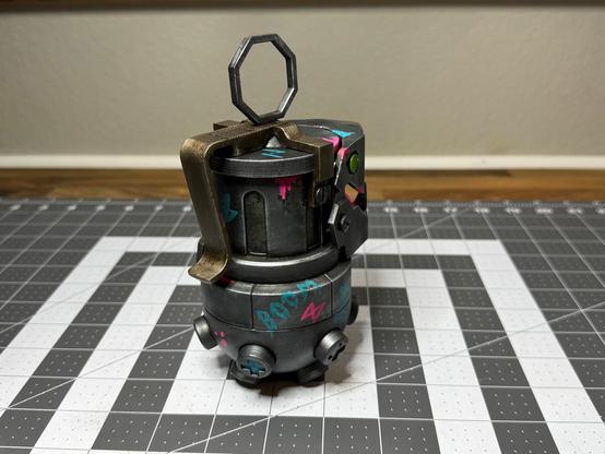 A 3D printed “Chompers” prop (grenade and bear trap combo) from League of Legends/Arcane. Has some neon “Jinx” style graffiti painted on it as well. (Rear other side view)