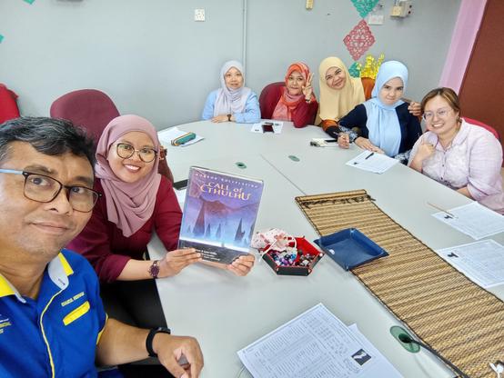 Some teachers pose for a photo around a meeting table with the Call of Cthulhu 5.5E rulebook, a dice tray full o' dice and character sheets.
