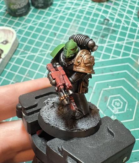 A Salamanders Adherent for Warhammer Horus Heresy. His head and right shoulder are green. His left shoulder is a gold salamander. He is holding a red combiflamer with a chain bayonet. His armor is black. 