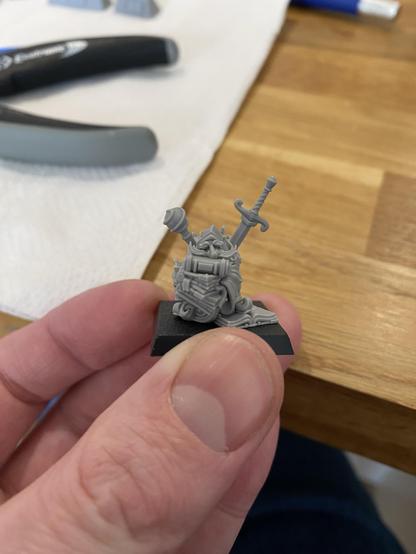 Small unpainted resin miniature Gnome with a sword, a staff, and peering over over a pile of books.
