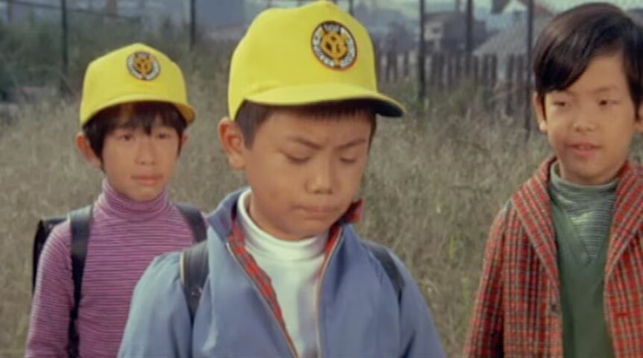 Two kids in a Godzilla movie wearing yellow ballcaps, like they're on a field trip.