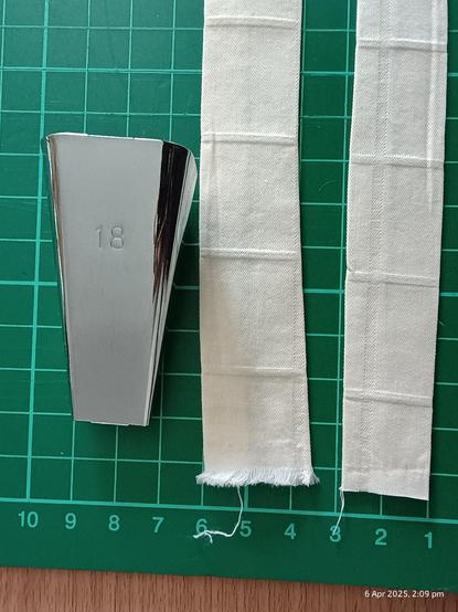 2 strips of cream coloured bias tape with folded sides down, on a green cutting mat with centimeter number markings.

Metal Bias tape maker with number 18 is alongside strips.
