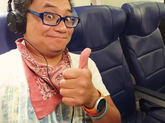 Jay giving a thumbs up, sitting in an airplane with a row all to himself