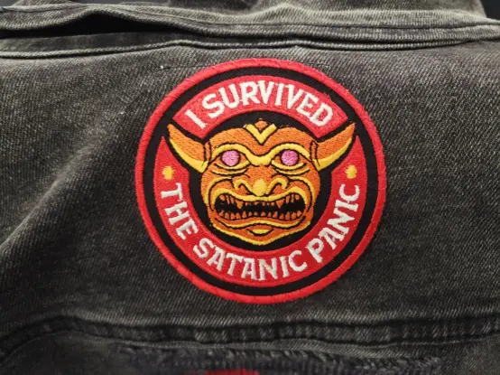 A patch depicting the eidolon statue from the D&D 1st edition Players Handbook, surrounded by the phrase, "I survived the Satanic Panic"