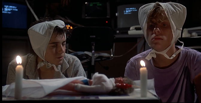 Scene from Weird Science.
2 teenagers with bras on their heads, with candles and a doll.
Computers in the background.