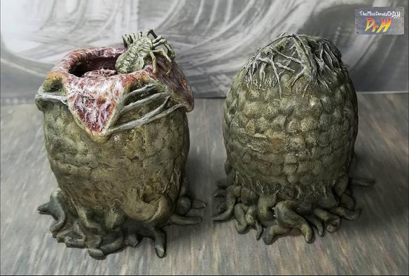 A pair of Alien eggs. One open with a facehugger emerging. Lower angle from the rear.