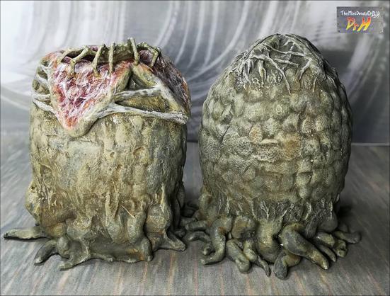 A pair of Alien eggs. One open with a facehugger emerging. Low angle from the front.