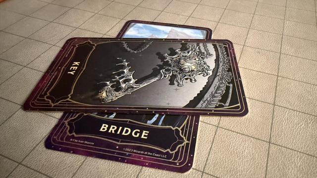 Two cards from the Deck of Many Things - The Key (an ornate silver key) and the Bridge (artwork obscured by the Key).