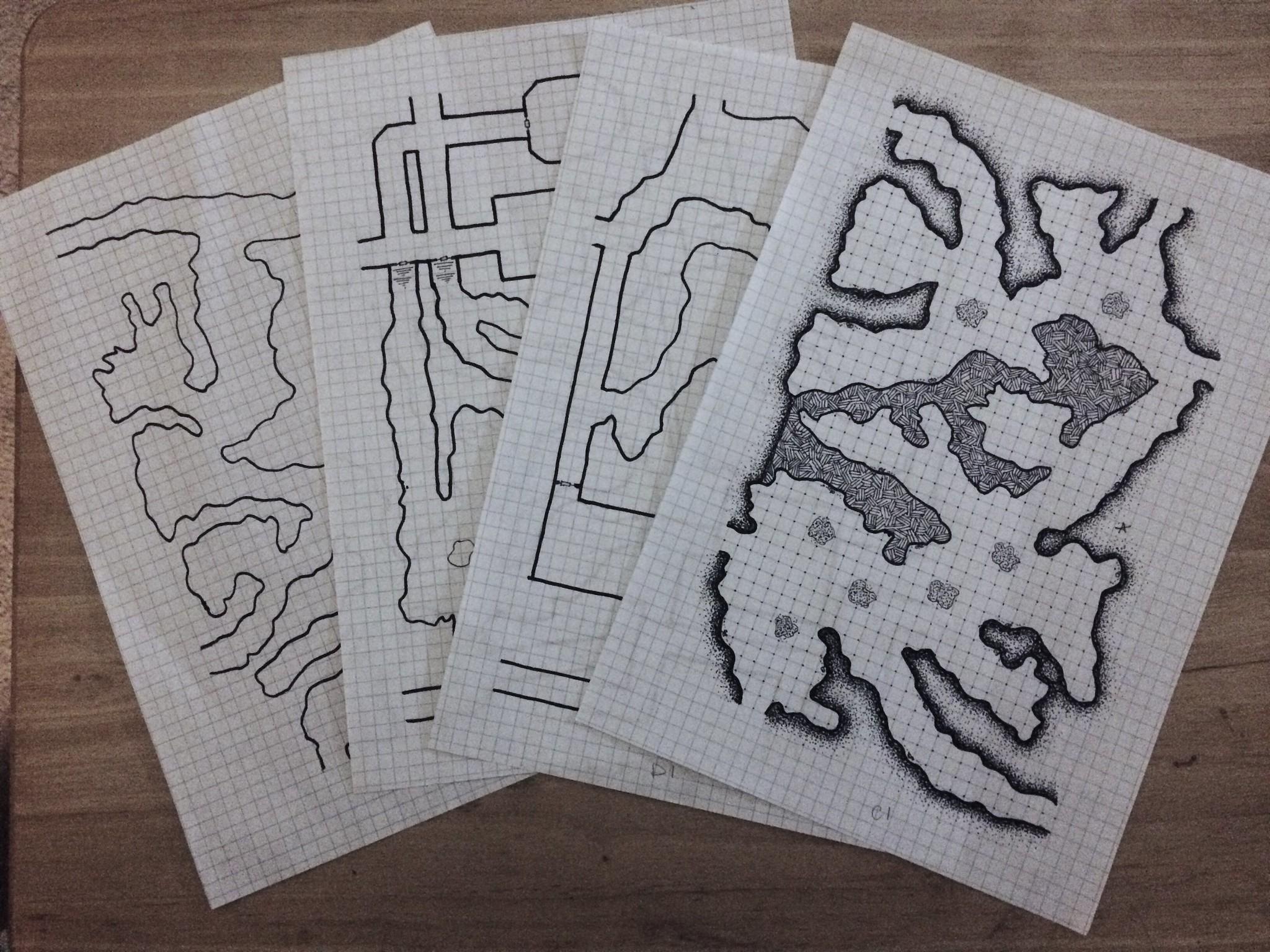 photo of several in progress dungeon/cave system maps in progress fanned out on a table. The top map is mostly complete with stippling shading and hashed fill done, the others are still outlines with no shading or hashing.