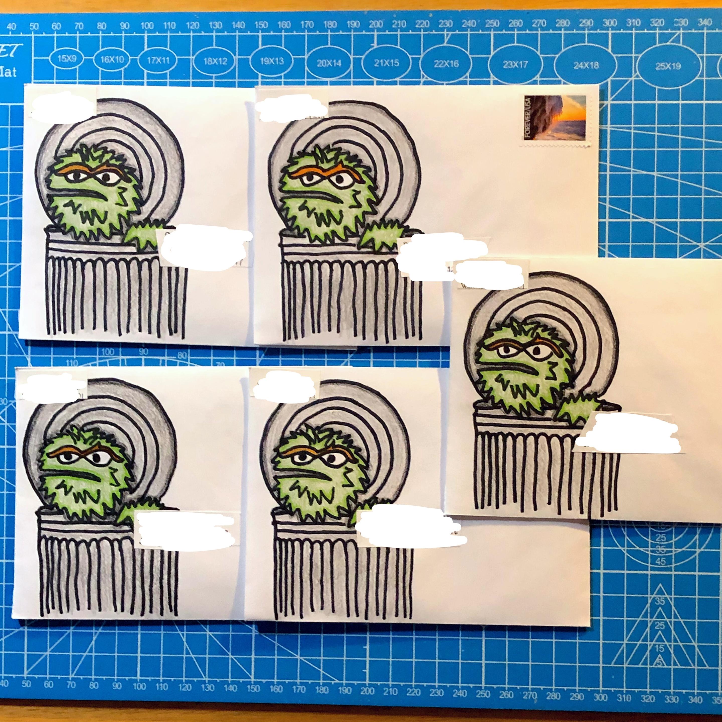 several white, hand made envelopes laid out on a blue cutting mat.
each envelope has a hand drawn and colored picture of Oscar the Grouch - a grumpy looking, matted, shaggy, green pea colored muppet with orange eyebrows - looking out of his trash can.