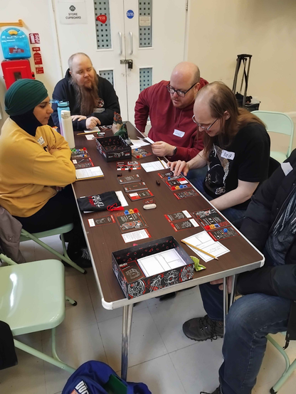 Table of players for a game of One Last Fight, with character sheets, game cards and coloured dice in use.
