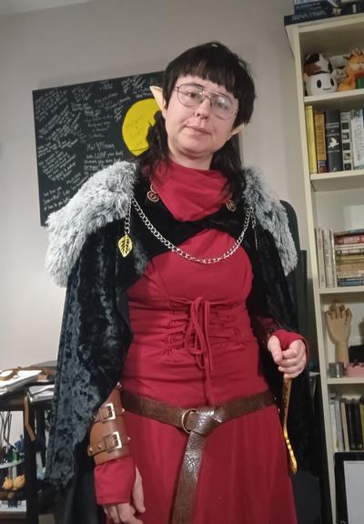 A cosplay selfie in fantasy garb. A red tunic dress with a black velvet cloak. Elf ears and a leather belt.