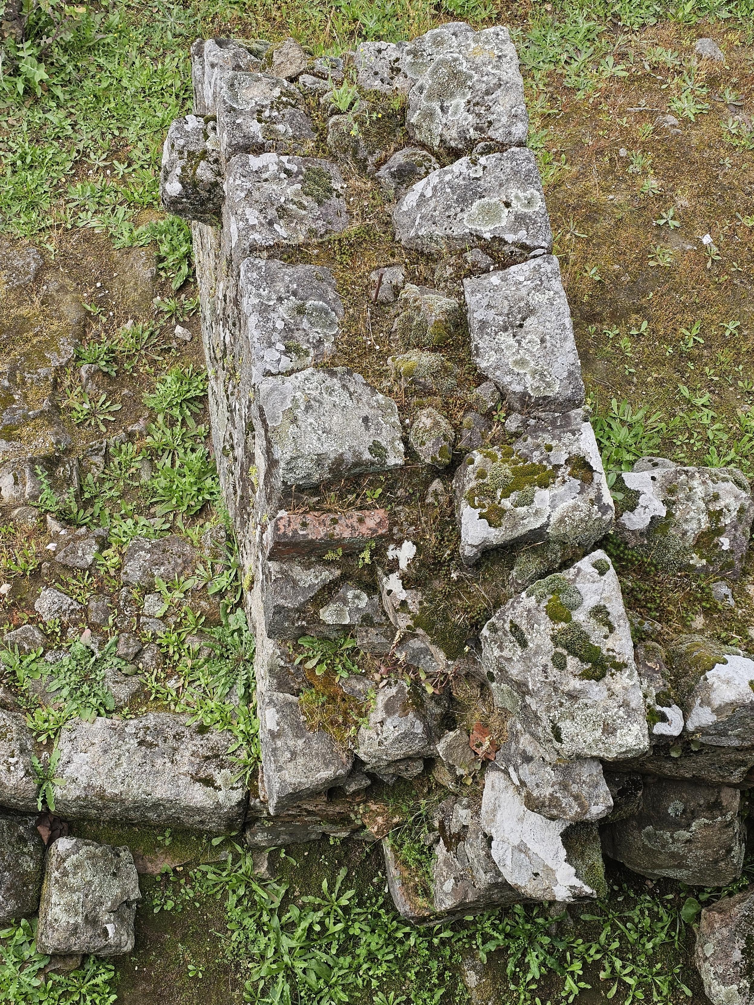 A low wall made of grey and white rock, about 2 feet tall, covered in green and brown mosd and splashes of lighter lichen.