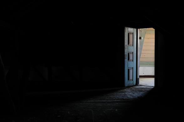 An open, timber door, as seen from inside a darkened room.