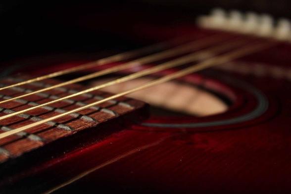 A closeup of the outside top of an acoustic guitar, showing its strings suspended across its sound hole.