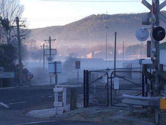 A photograph of Bowenfels level crossing (near Lithgow, NSW, Australia), taken by me (David M Jacobs) on the morning of June 4, 2015.

A tarred road crosses a railway track, surrounded by road signs, crossing signals, chain-link fences, timber power poles, and other miscellaneous industrial ground cover. Everything in the foreground is shadowed and coated in frost. Mist obscures the middle ground, and a thawing mountainside looms in the distance, its thick carpet of eucalypts drinking in the me…
