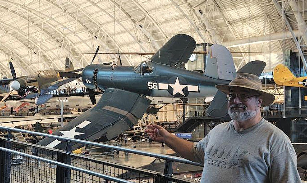 Doofy looking old white guy in beard, glasses, and a brimmed hat standing on the right gestures with his hand toward the left where a Vought F4U-1D Corsair hangs from the museum hangar ceiling, a gull-winged blue fighter plane with a bubble canopy cockpit and white US star and bars insignia on the fuselage and wing. The theme to Black Sheep Squadron courses through the man’s nostalgic mind….

https://airandspace.si.edu/collection-objects/vought-f4u-1d-corsair/nasm_A19610124000