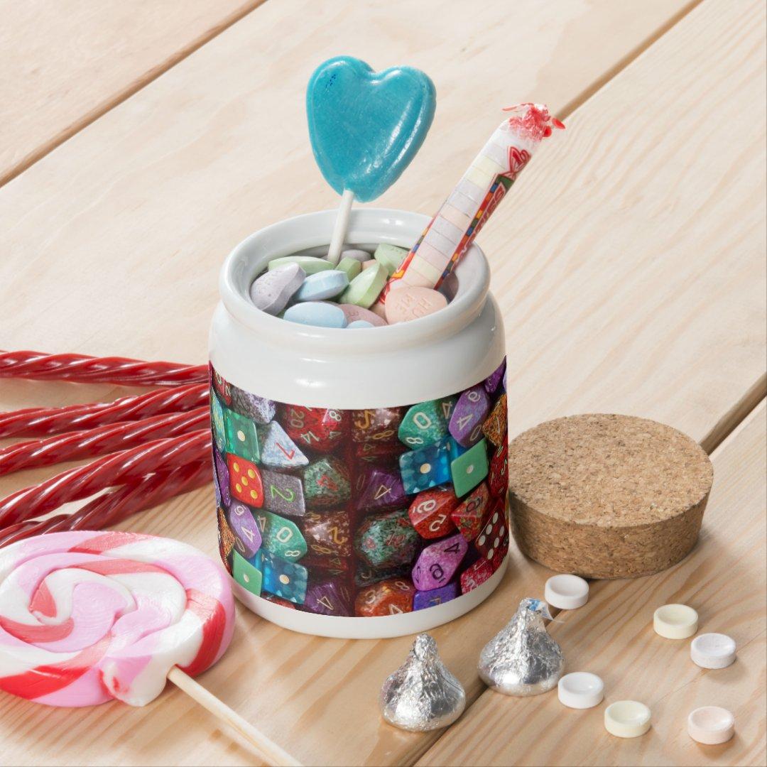 product image of a small ceramic candy jar with a large cork stopper/lid surrounded and filled with various types of candy. The image on the jar is a wraparound image of a pile of multi colored multi sided dice.