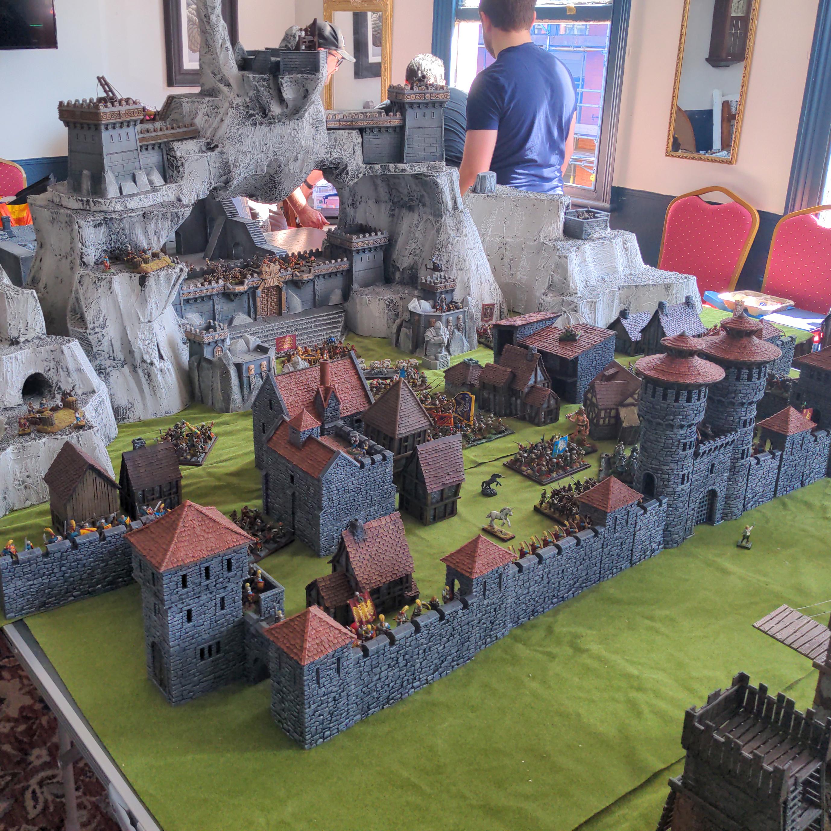 A close up shot of the fortress showing the outer wall and town in front of  the mountain hold behind.