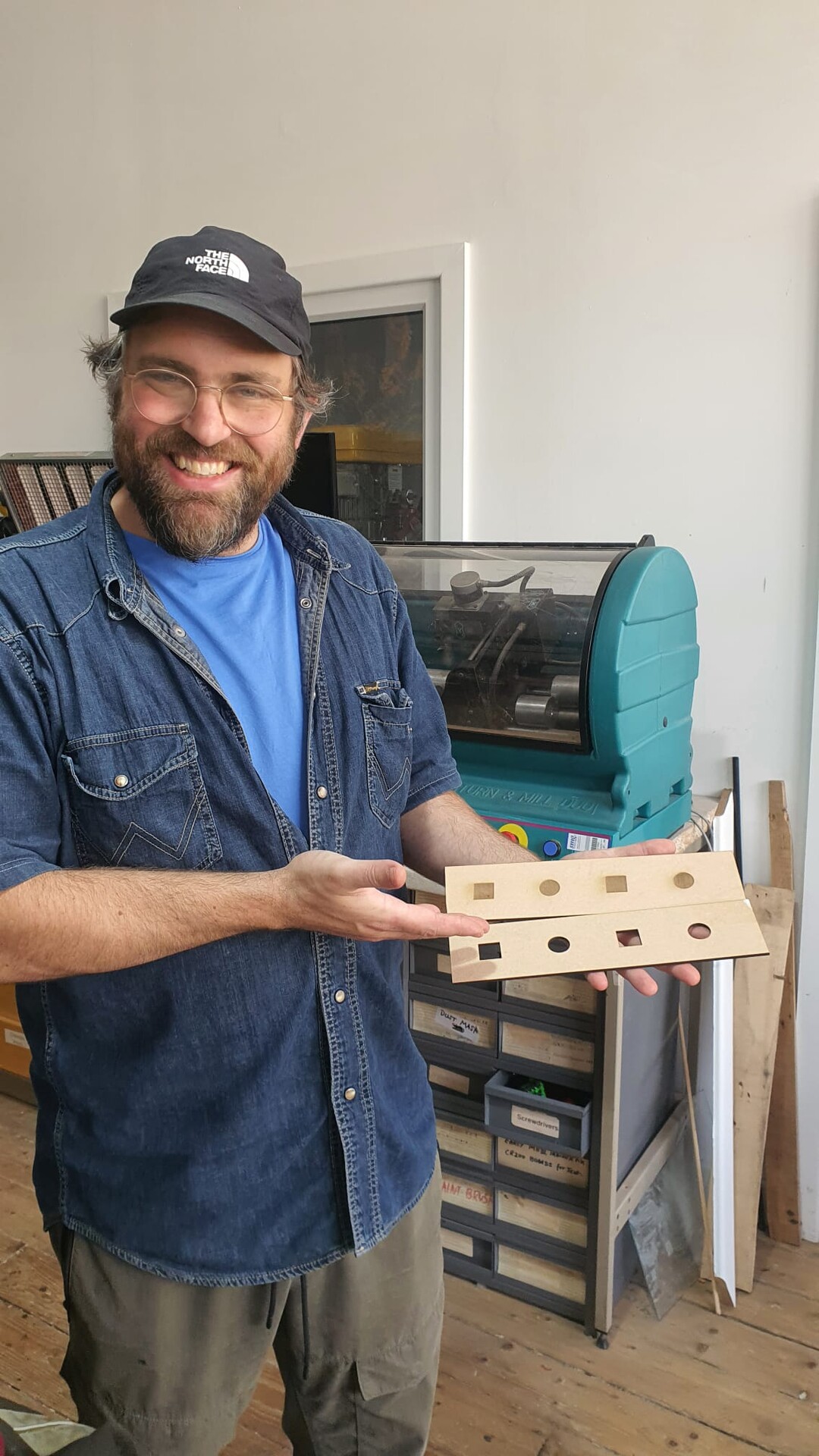 A smiling person holding up pieces of MDF with test laser cuts and engraves
