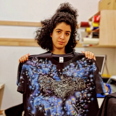 Niloo holding up a black t shirt with hand painted, airbrushed and screen printed elements 