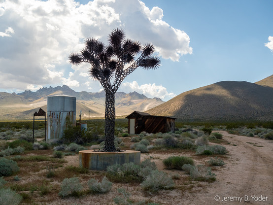 A disused mining site with a shed and a water tank and, for some reason, a metal sculpture of a Joshua tree on a concrete base