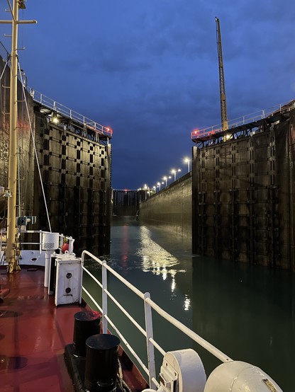 Photo from bow of ship of canal lock doors opening to allow the ship to progress through. It is near nightfall and the canal is lit by lights.
Photo from H Niblock, DFO.