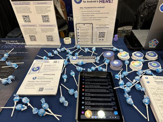 The Thunderbird booth table, decorated with stickers and blue candy, as well as flyers and tablets running the Android app.