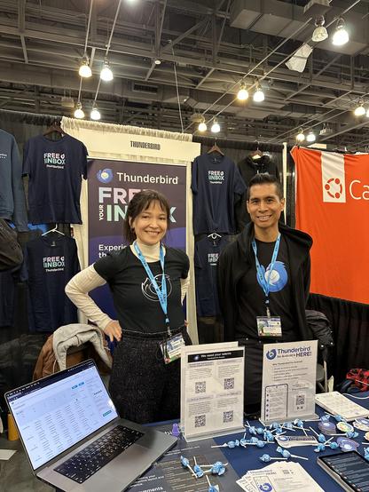 Natalie and Chris, two members of the Thunderbird team, standing at the booth and smiling.