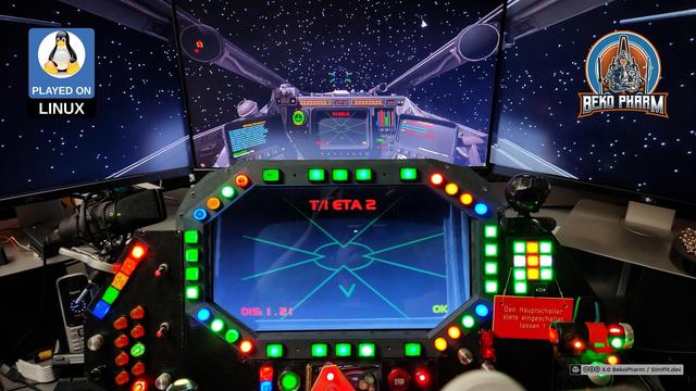 A home cockpit consisting of 3 monitors showing the game. The central space is used up by an elaborate button box with many lights and a central display. The targeting computer of the X-Wing is duplicated on a 4th monitor embedded in the centre of the button box.