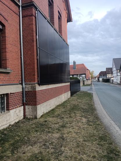 Eine Fassaden-Solaranlage und ein Solarzaun an einem roten Backsteinhaus.